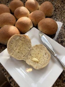 dinner rolls cut open with butter on a white square plate with a knife
