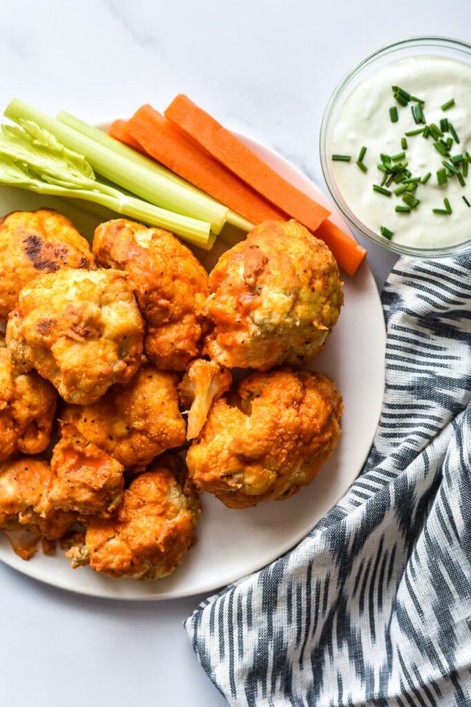 buffalo cauliflower pictured on a plate with celery and carrots with ranch dip