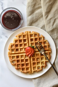 waffle made with manitoba milling company whole-milled flaxseed topped with a sliced strawberry on a white background