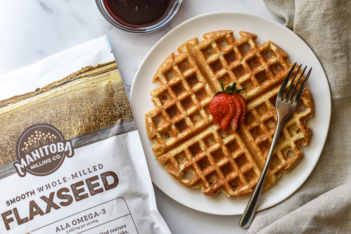 waffle on plate with strawberry on top pictured with Manitoba Milling Smooth Whole Milled Flaxseed bag