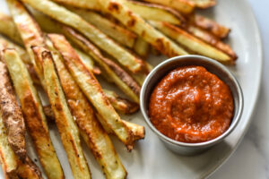 a close up photo of french fries with a silver ramekin filled with homemade ketchup