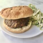 a photo of a hamburger on a bun with a side of coleslaw, bother are pictured on a white plate