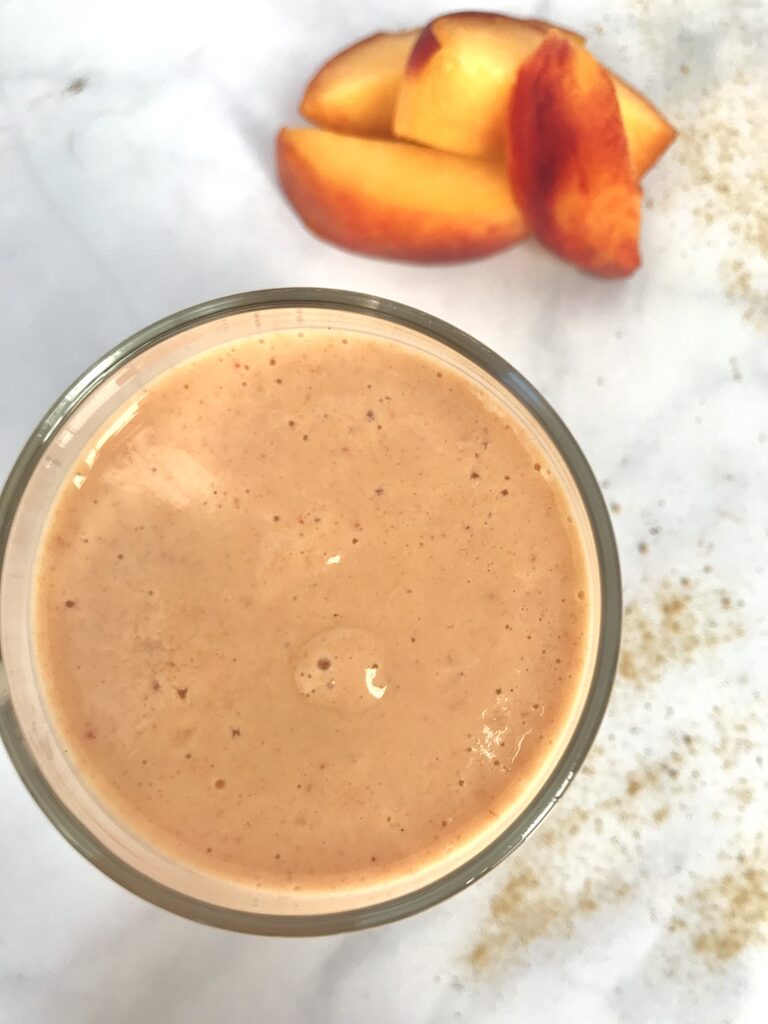 photo of a peach smoothie on a white background pictured with a small pile of sliced peaches