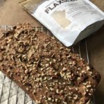 photo of zucchini bread topped with crumbled pecans on top,pictured on a cooling rack on top of a wooden cutting board