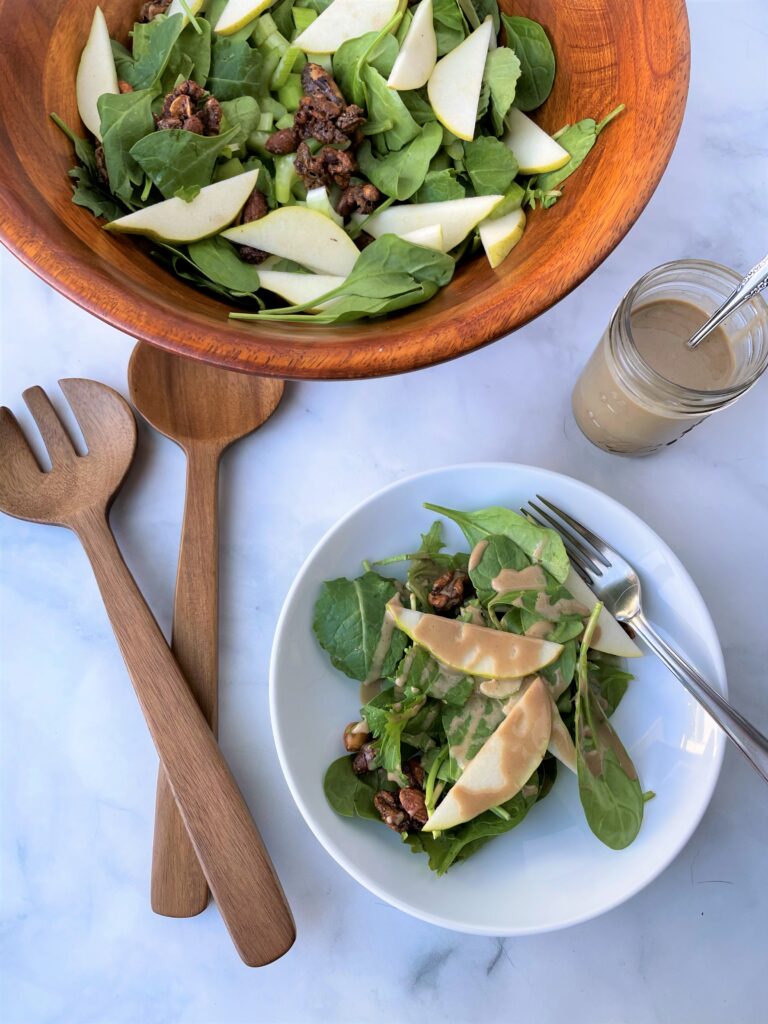 bowl of green salad with raisins and pears and a plate with the salad and the creamy balsamic vinegar dressing. 