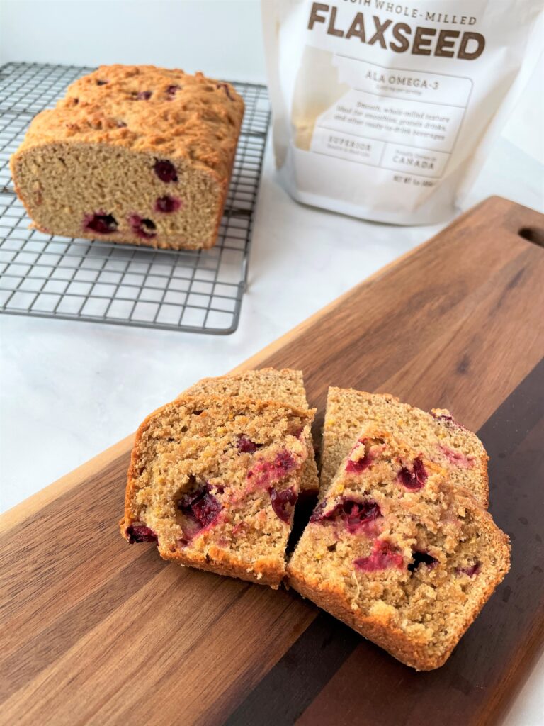 slices of cran-orange quick bread on a wooden tray with the rest of the loaf behind it.
