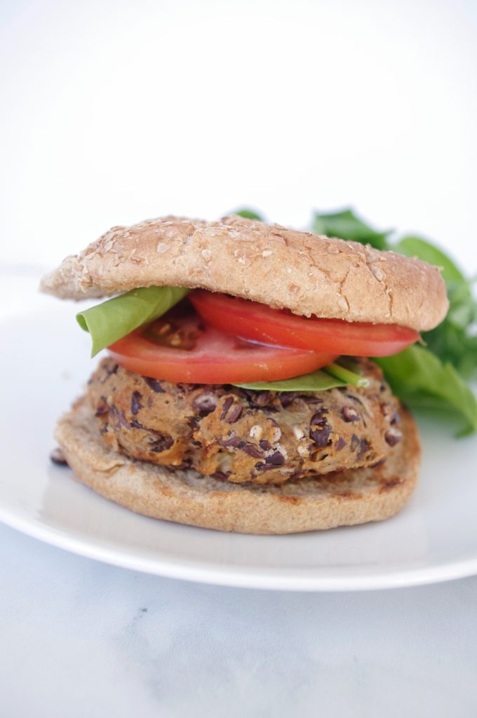 a photo of a black bean burger on a white plate, shown on a whole grain bun with tomato and lettuce