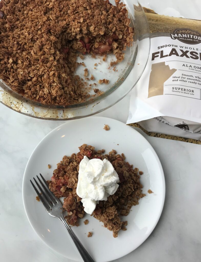 Plate of apple crumble next to the rest of the apple crumble dish and a bag of Manitoba Milling Flaxseed