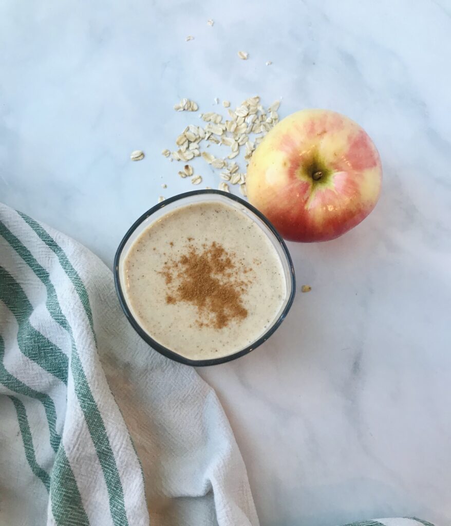 Apple pie smoothie in a cup next to a whole apple