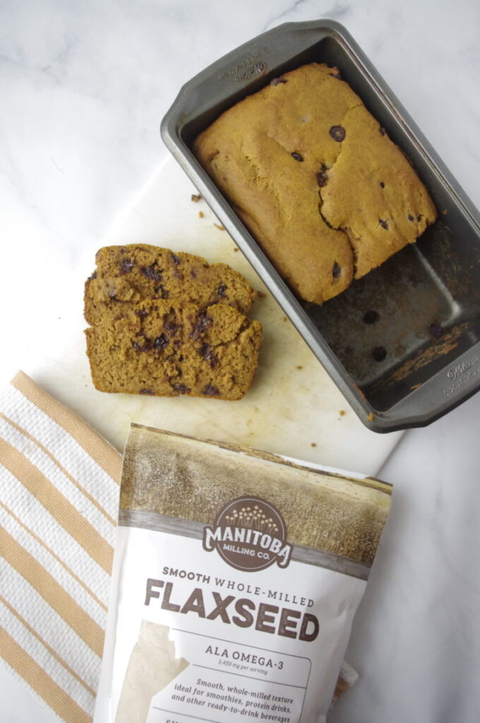 a loaf of pumpkin bread on a cutting board with a bag on Manitoba Milling smooth whole milled flaxseed next to it.