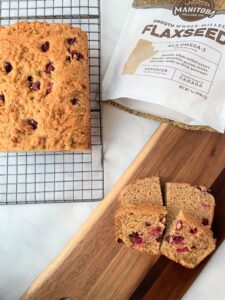 two slices of cran orange bread on a wooden tray with the rest of the loaf on a cooling rack behind