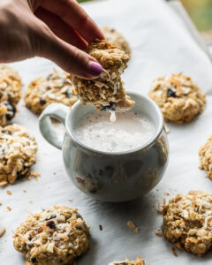 oatmeal fruit and nut cookie made with manitoba milling company whole-milled flaxseed being dipped into a blue mug filled with flax beverage